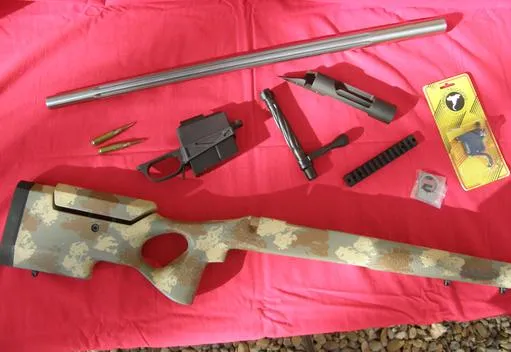 Rifle action, barrel, stock, bottom metal and rail laid out before assembly